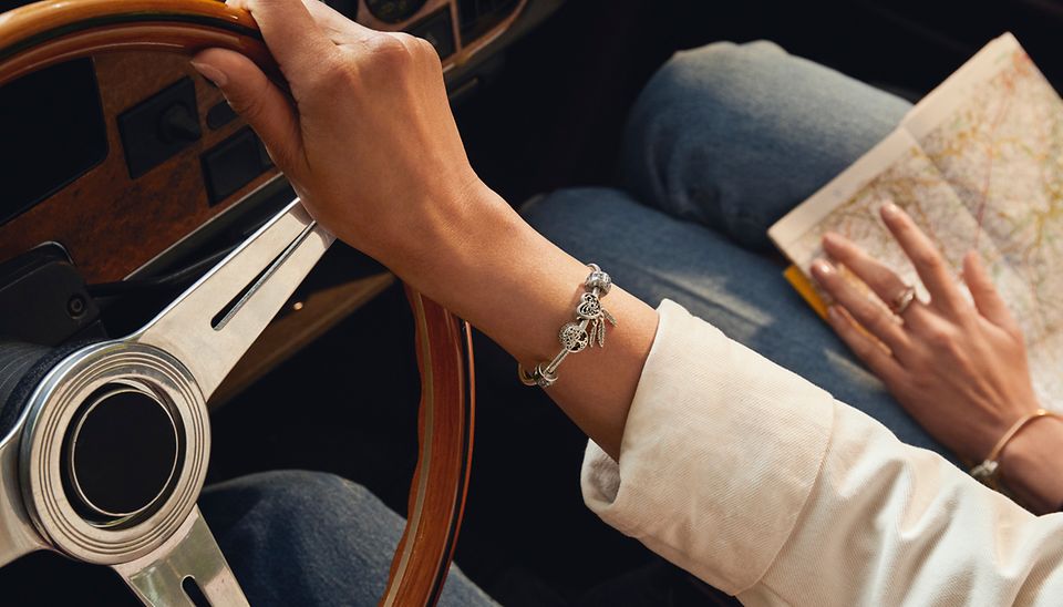 Bracelet Pandora Moments porté avec des charms sur le thème du voyage