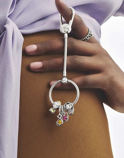 Modella che tiene in mano una base per charm per borsa in argento sterling 925 completo di charm della collezione Disney x Pandora