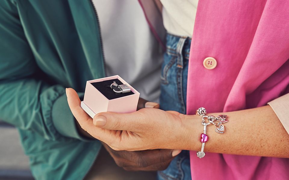 Hand wearing bracelet with charms holding a jewelry box with a charm