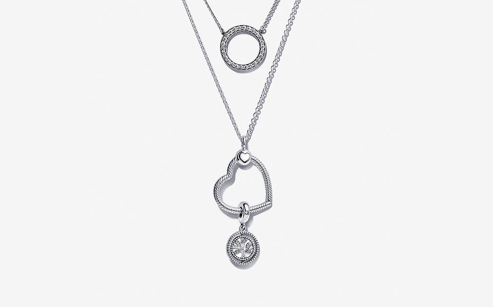 Drei Halsketten im Lagenlook, darunter eine Halskette mit Strahlenkranz, eine Pandora O Pendant Halskette und eine Herzanhänger-Halskette mit einem Charm