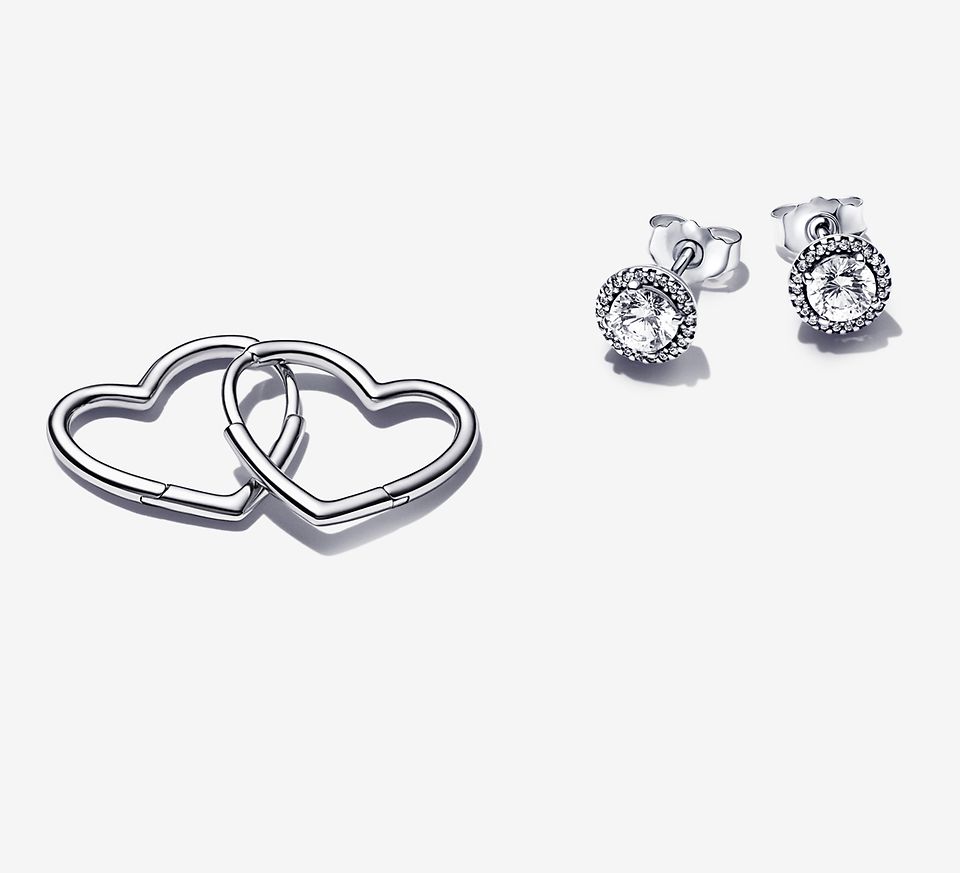 Trzy rodzaje srebrnych kolczyków, w tym koliste sztyfty, obręcze w kształcie serc i okrągłe, lśniące sztyfty