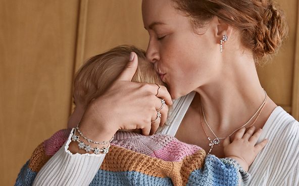 Mamma som bär Pandoras mors dag-smycken, kramar ett barn och pussar huvudet