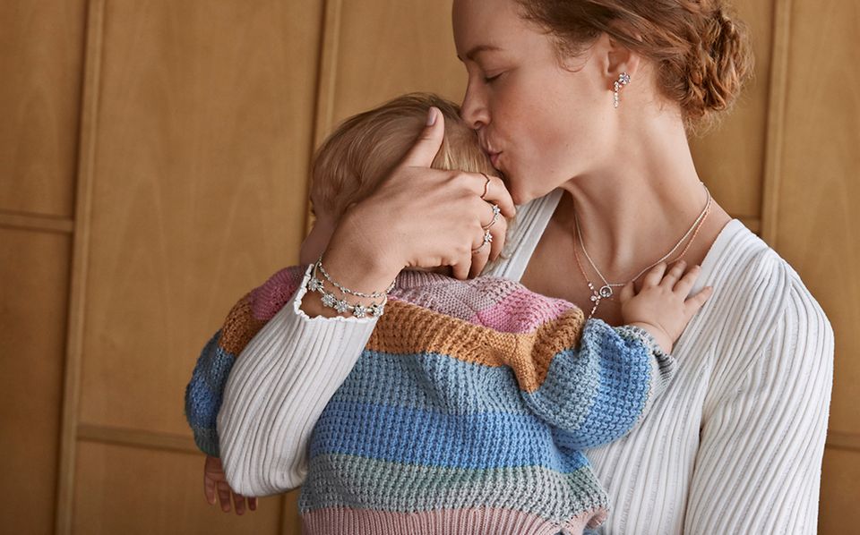 Mother wearing Pandora Mother's Day jewellery cuddles baby and kisses the head