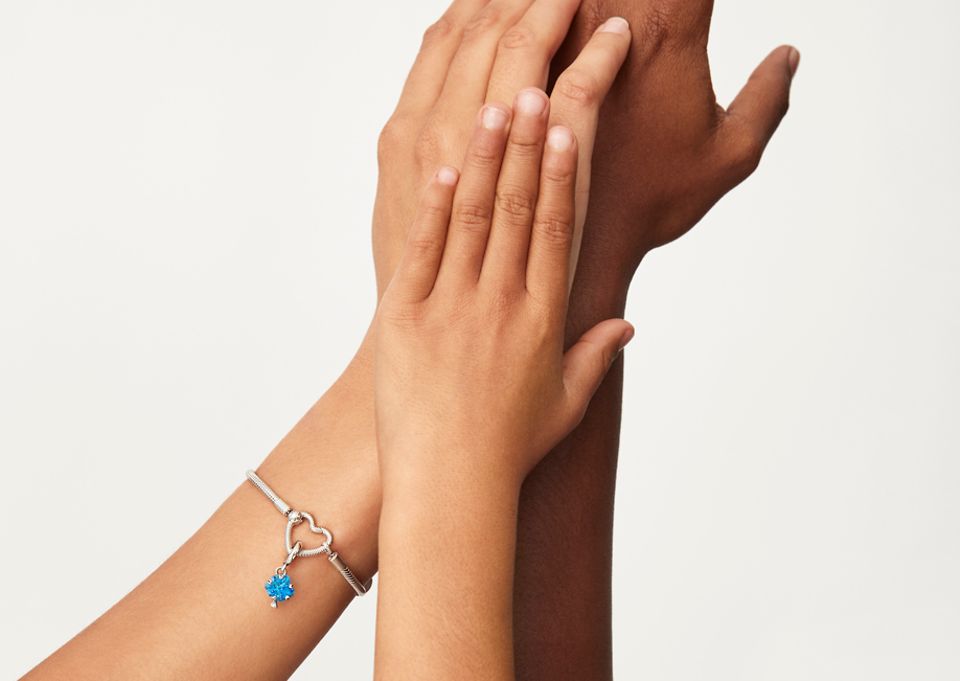 Bras d'un enfant levé avec les bras d'un adulte, l’un portant un bracelet Pandora pour Unicef