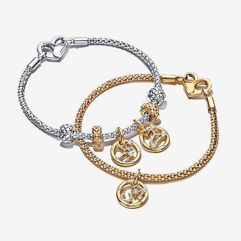 Immagine di un bracciale con placcatura in Oro 14k con charm Pandora Moments ispirati allo zodiaco indossato sopra un bracciale in Argento Sterling 925