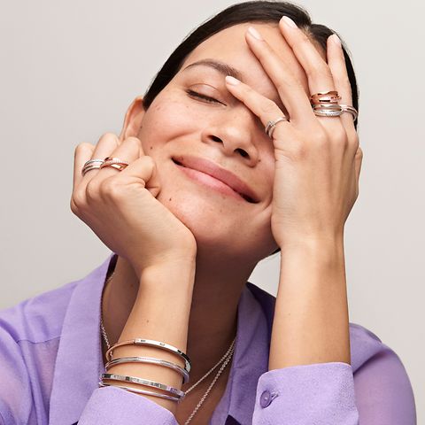 Kobieta w fioletowej koszuli nosząca pierścionki do łączenia i bransoletki Pandora Signature