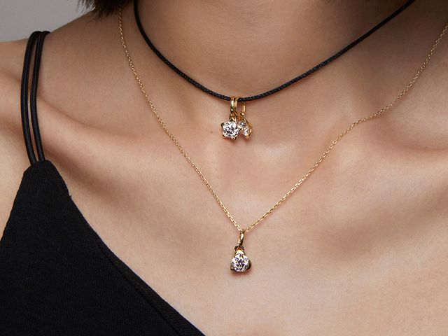 Woman wearing 2 lab grown diamond pandora talisman necklaces, 1 gold and 1 black