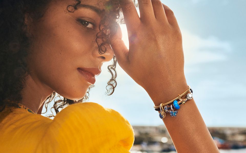Smiling woman with colourful blue charms on bracelet.