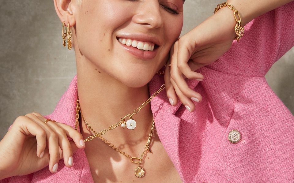 Mujer sonriendo llevando collares, pendientes y una pulsera con recubrimiento de oro de 14k de Pandora ME.