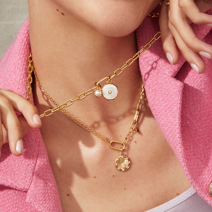 Kvinnan ler och bär guldhalsband, örhängen och armband ur Pandora ME-kollektionen.