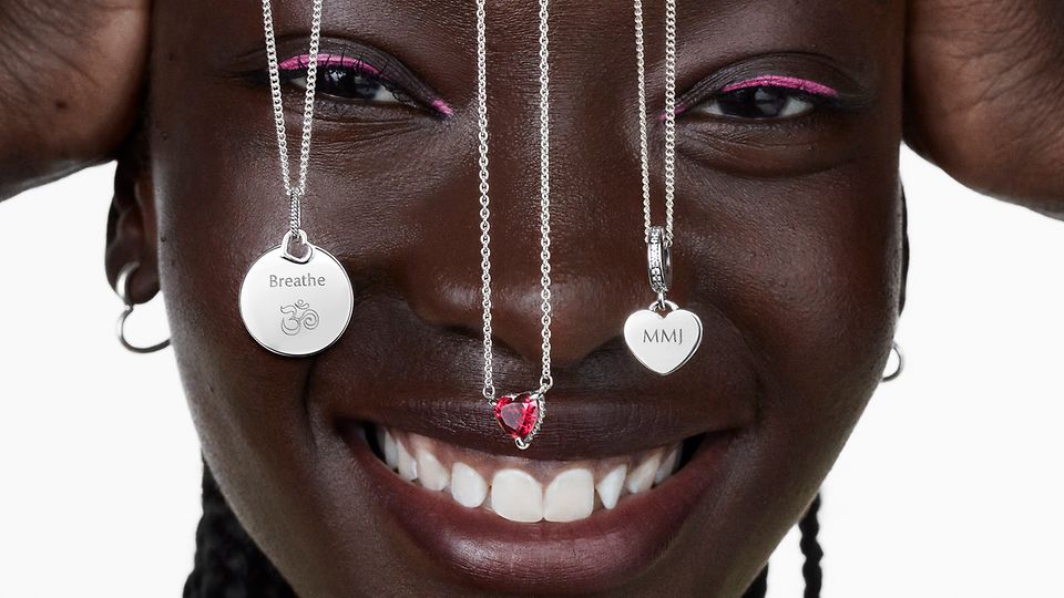 Donna sorridente con tre collane Pandora in argento che le pendono sul viso