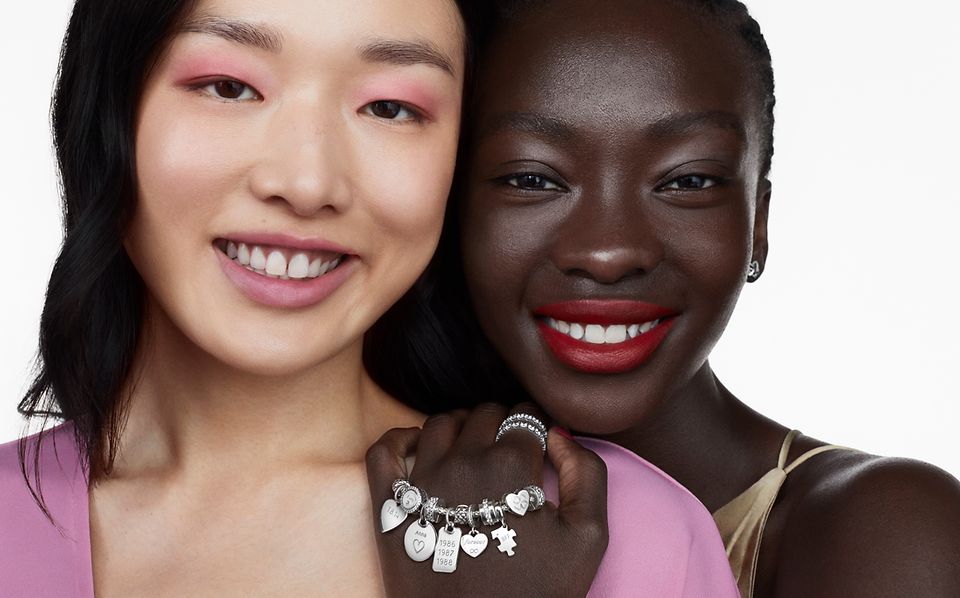 Two women smiling, one wearing a silver Pandora bracelet, rings and earrings 